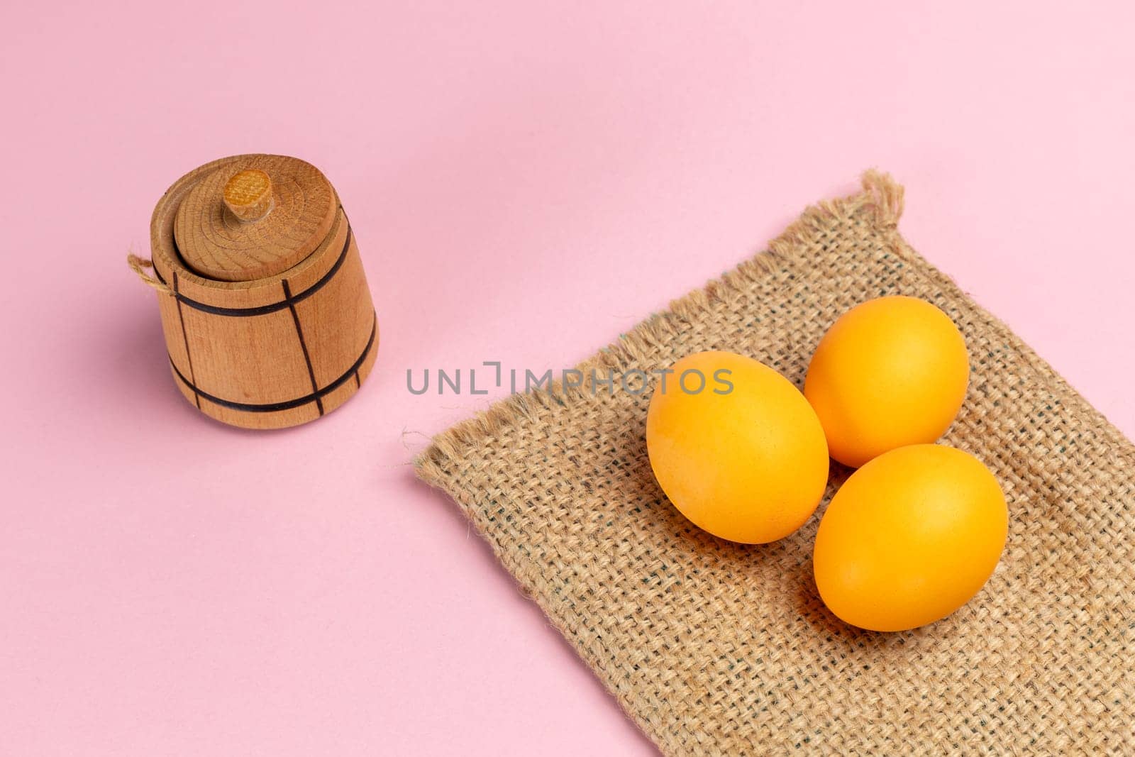 Yellow Easter eggs on the sackcloth bag with the pink background. Top view with a copy space.