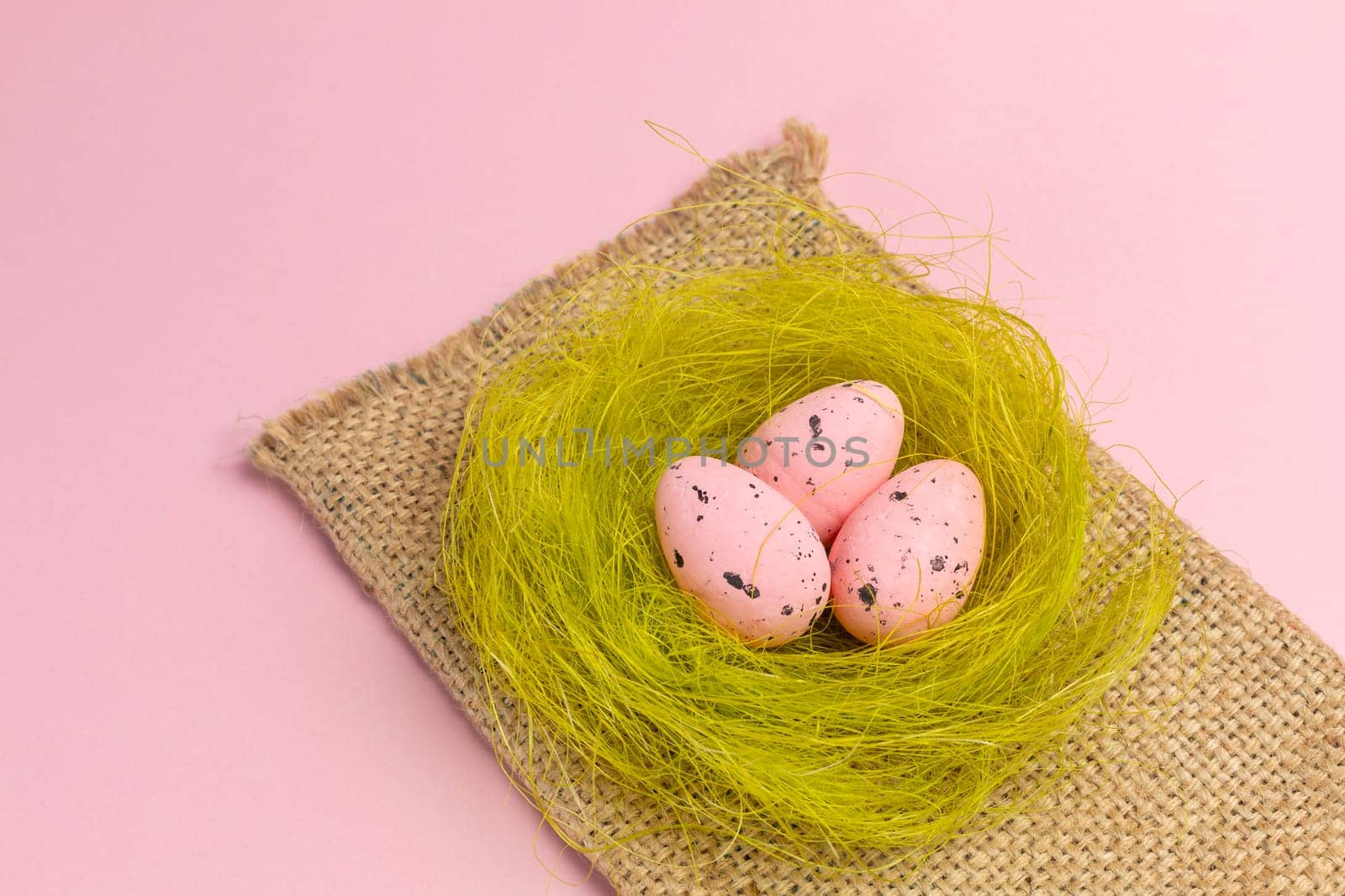 Nest with colored Easter eggs on the sackcloth bag with the pink background. Top view.