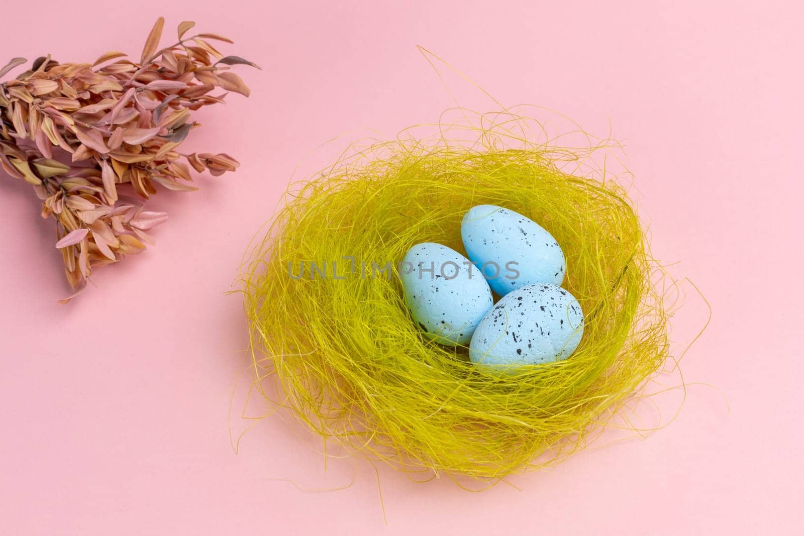 Nest with colored Easter eggs on the pink background with decor plants. Top view.