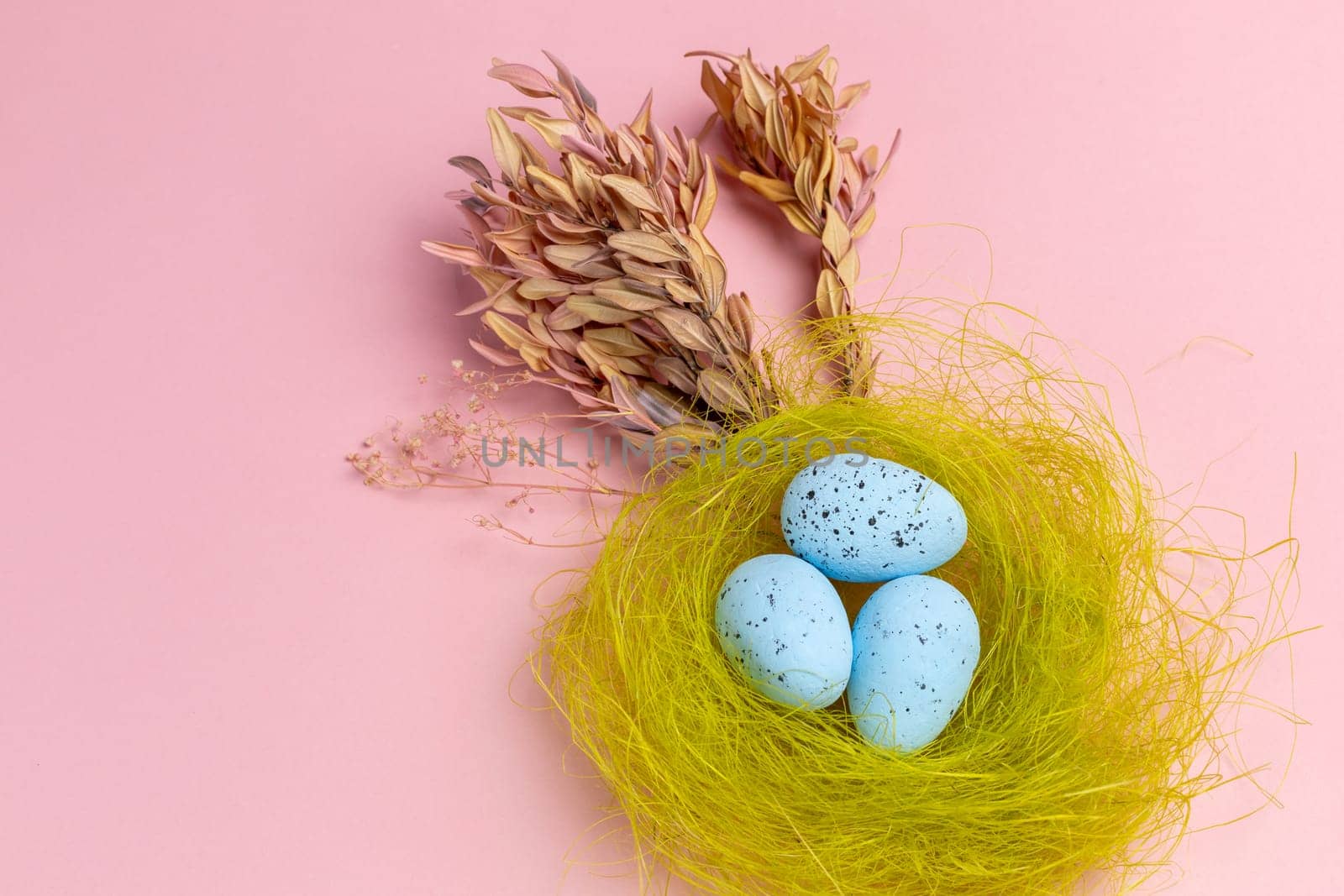 Nest with colored Easter eggs on the pink background with decor plants. Top view.