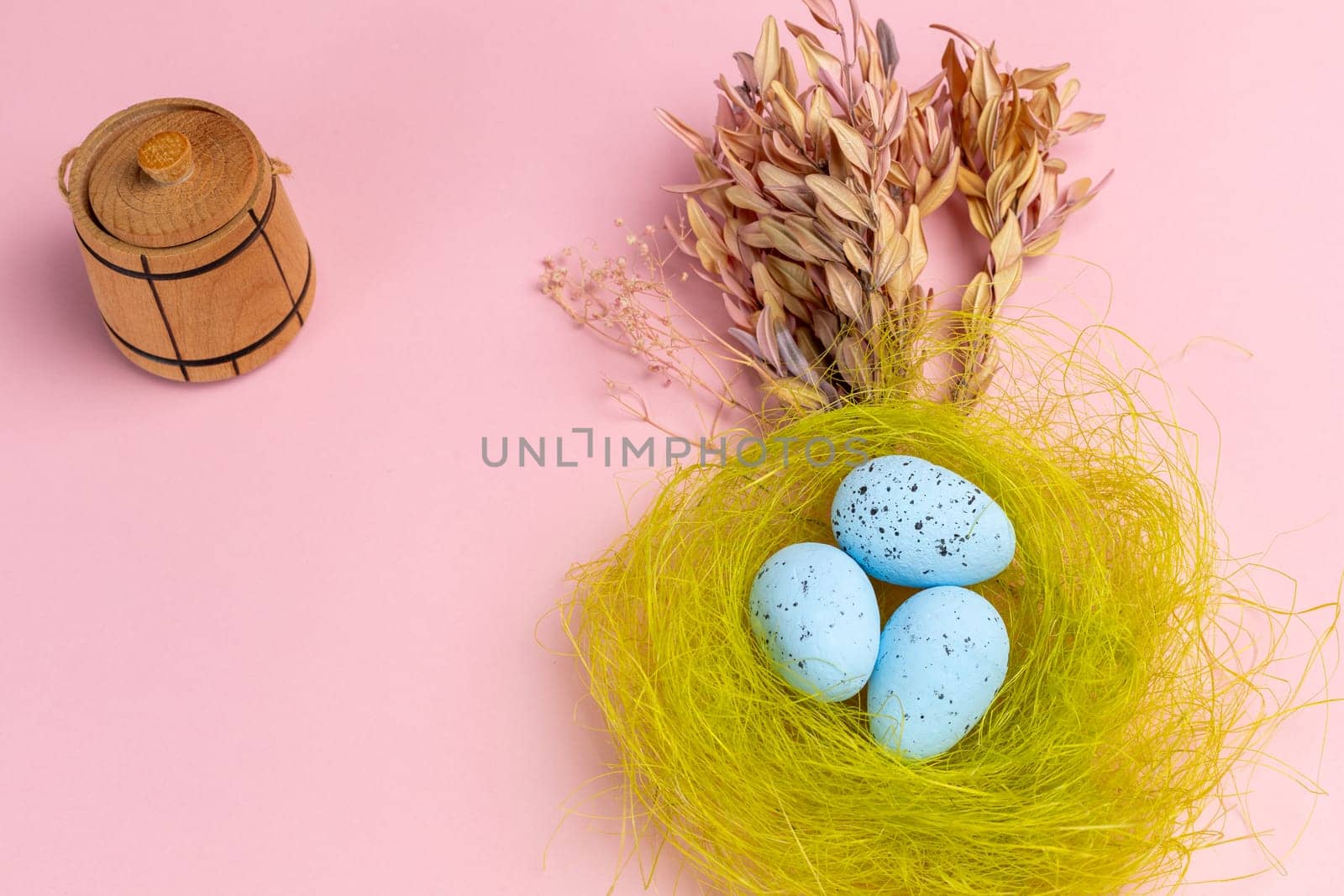 Nest with colored Easter eggs on the pink background with decor plants and wooden utensil. Top view.