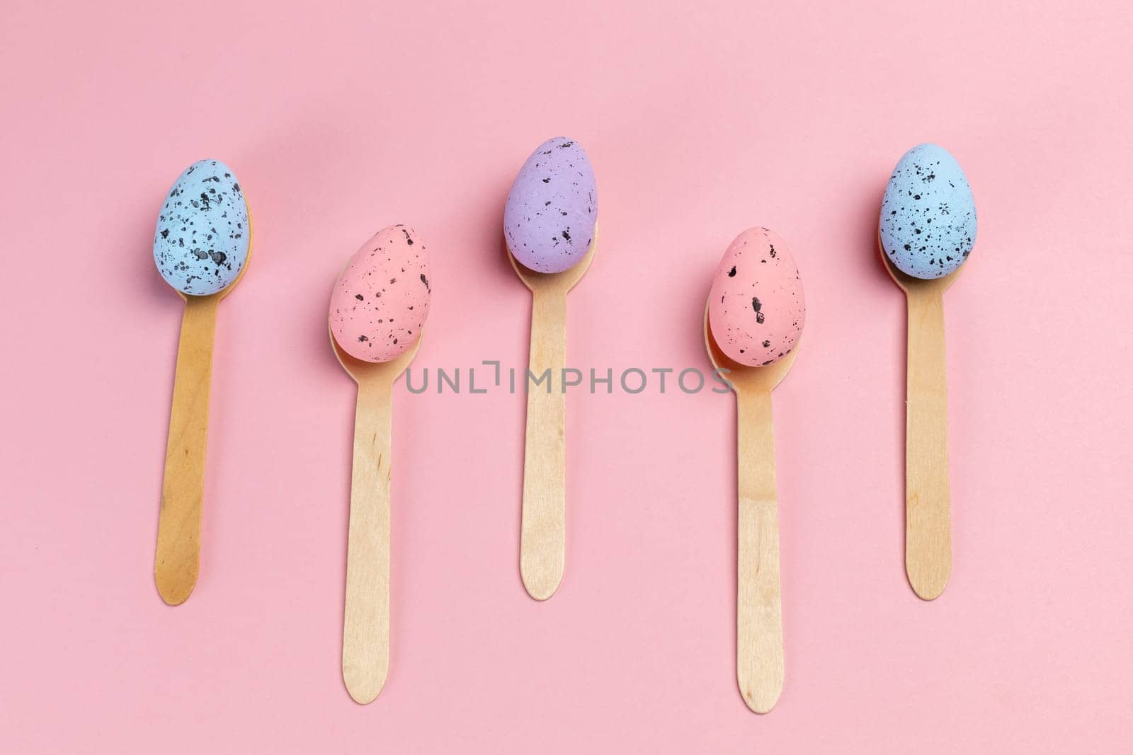 Colored Easter eggs with the wooden spoons on the pink background. Top view.