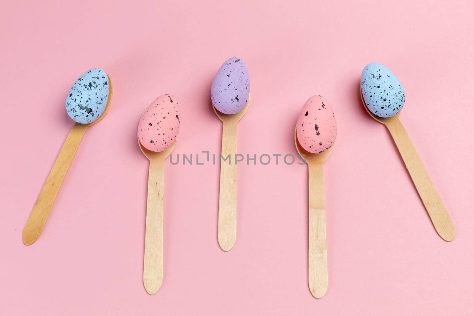 Colored Easter eggs with the wooden spoons on the pink background. Top view.