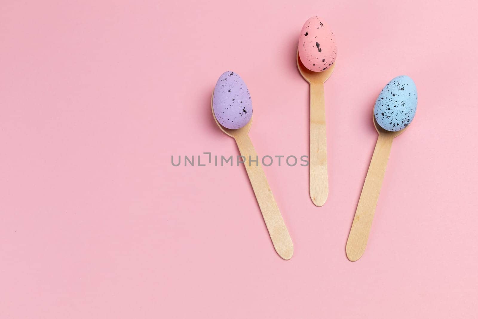 Colored Easter eggs with the wooden spoons on the pink background. Top view.