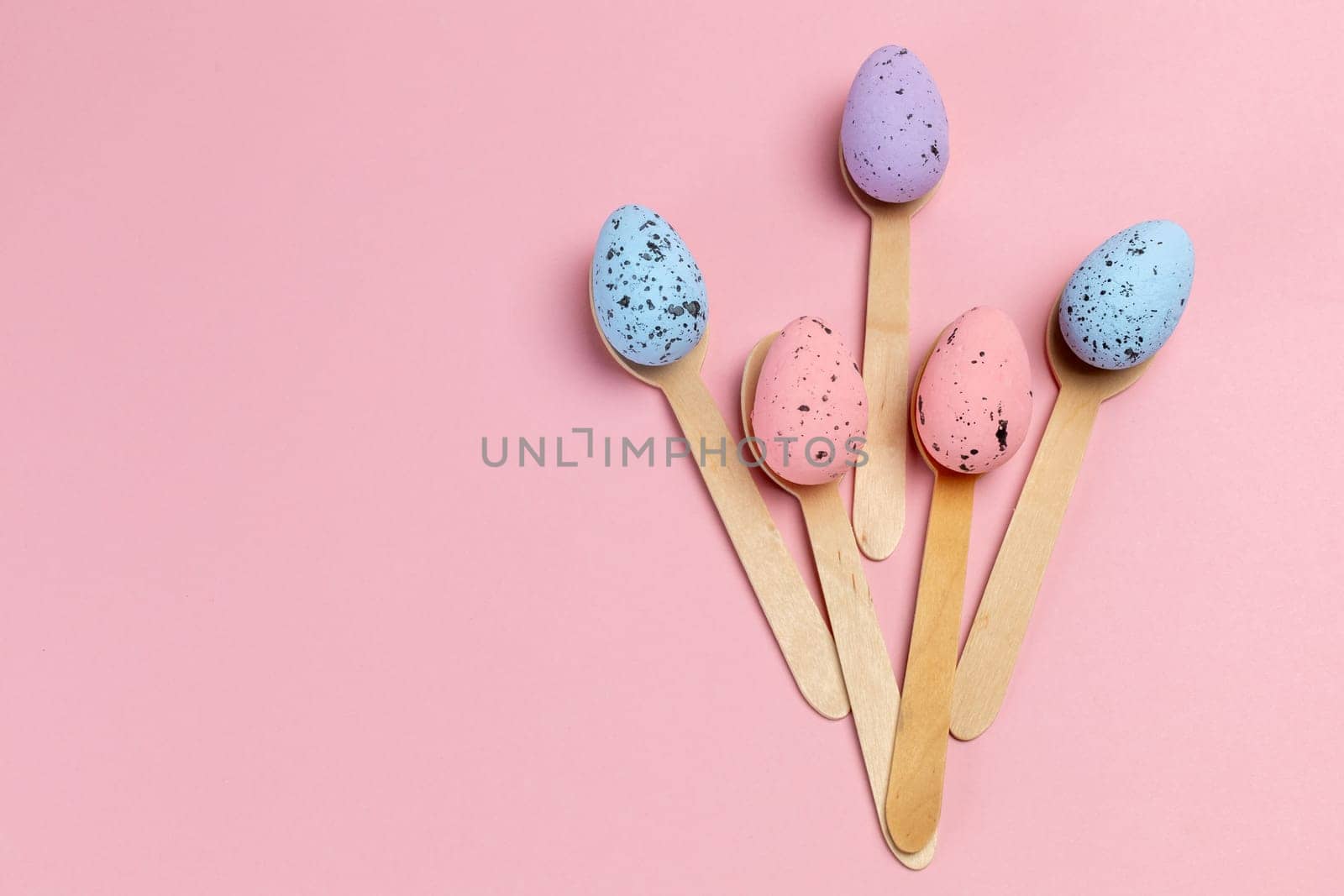 Colored Easter eggs with the wooden spoons on the pink background. Top view.