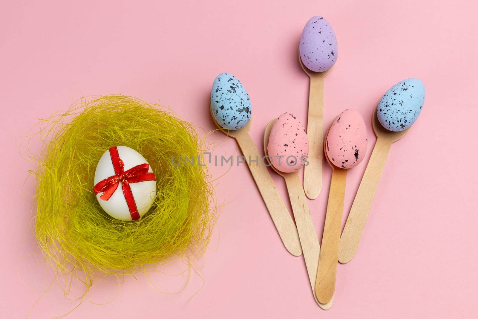 Colored Easter eggs with the nest and the wooden spoons on the pink background. Top view.