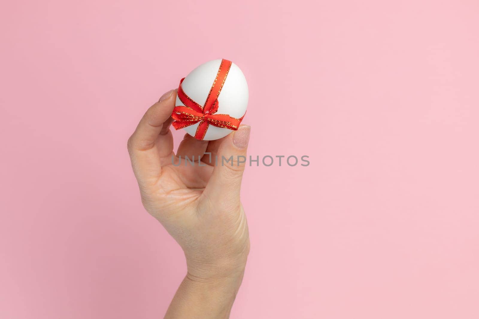 Woman is holding the Easter egg tied with a red ribbon on the pink background. Top view.