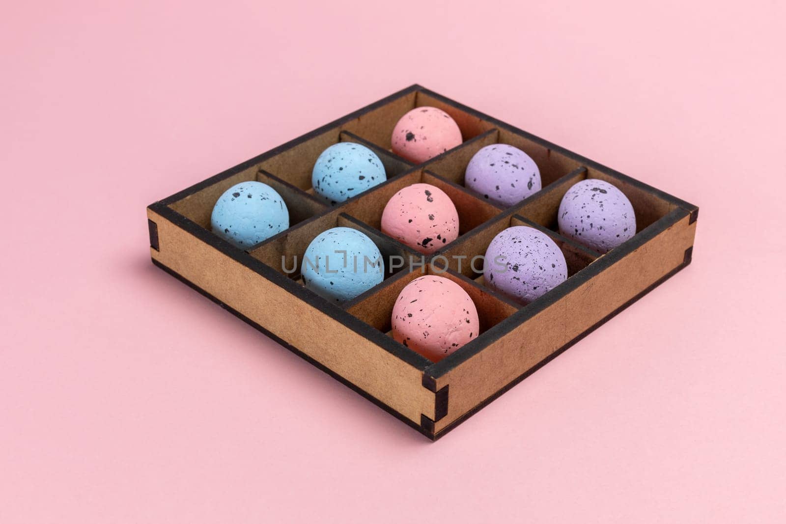 Colorful Easter eggs in a wooden box on the pink background.