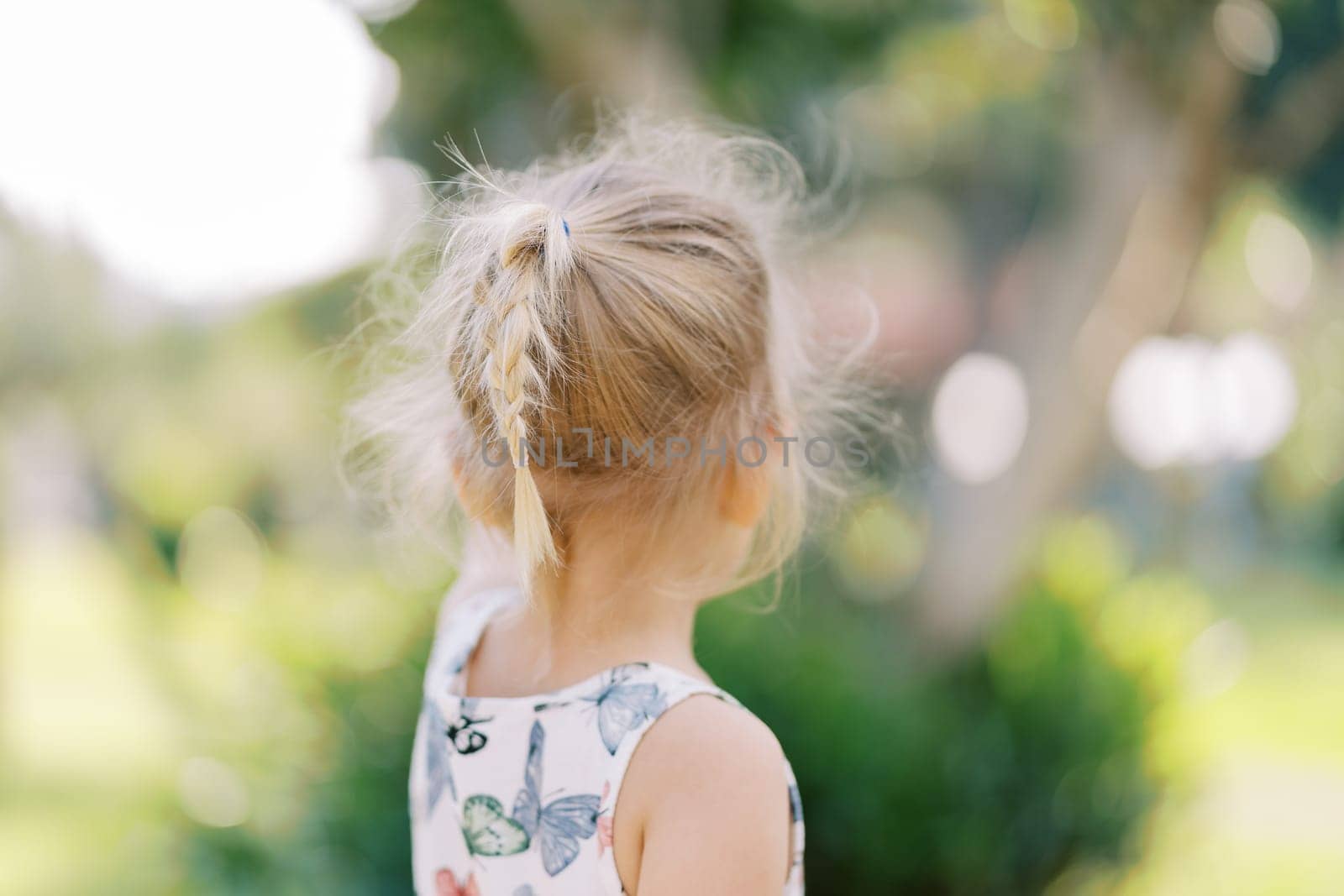 Little girl with flowing hair stands near a tree and points to it. Back view. High quality photo