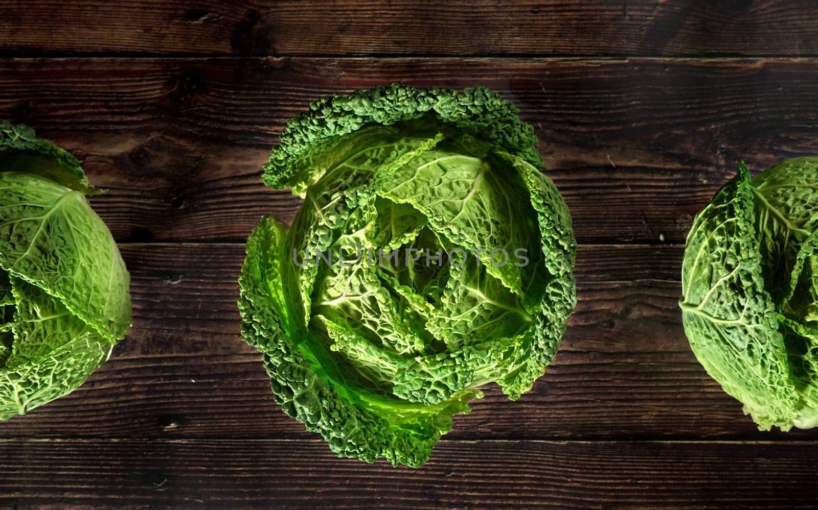 Green savoy cabbage lettuce heads on dark wooden board, view from above