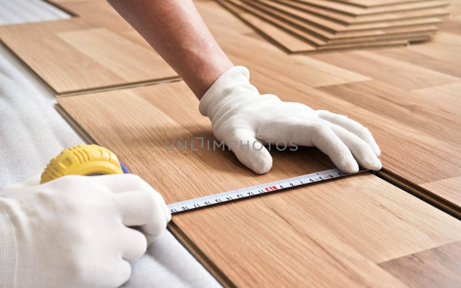 Installing laminated floor, detail on man hands in white gloves holding measuring tape over wooden tile by Ivanko