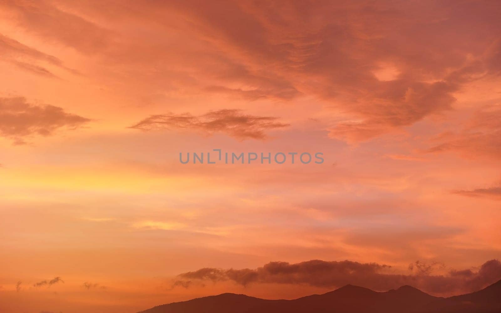 Calm orange and pink sunset sky, silhouettes of mountains below - can be used as background with subjects placed in front