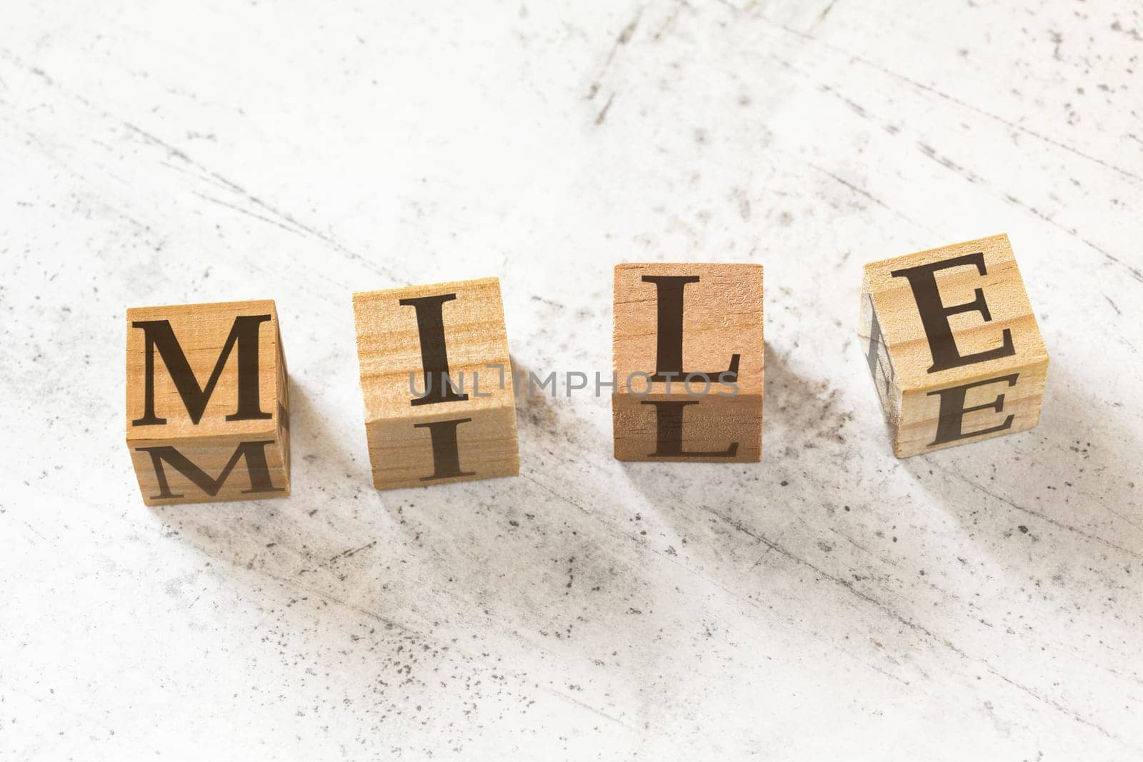 Four wooden cubes with letters MILE (meaning Maximum Impact Little Effort) on white working board.