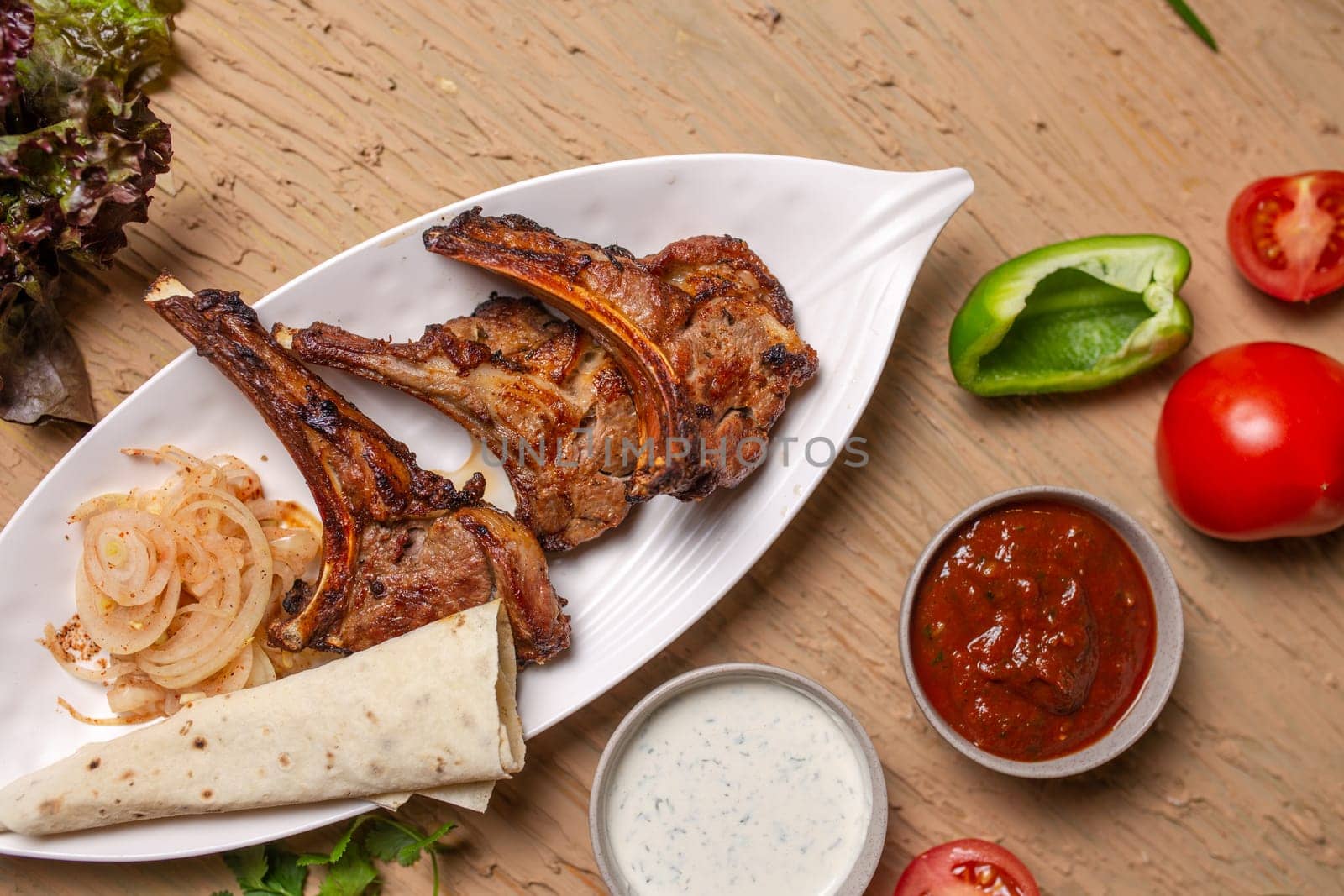 Grilled lamb chops with vegetables and lavash bread on a wooden table by Pukhovskiy