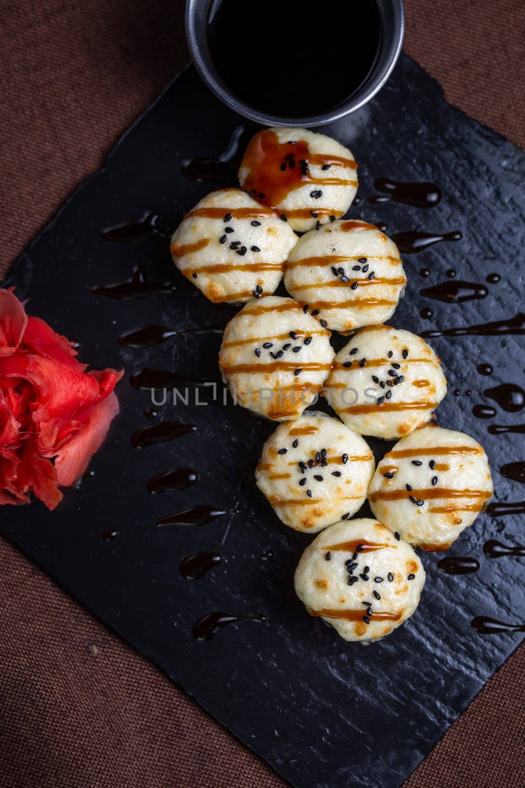 Japanese cuisine, rolls with cheese and sesame seeds and soy sauce on a black plate.