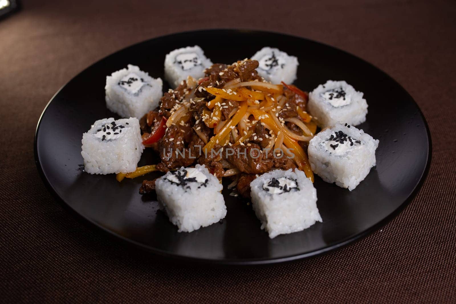 Japanese cuisine, rice rolls with sesame seeds and soy sauce on a black plate.