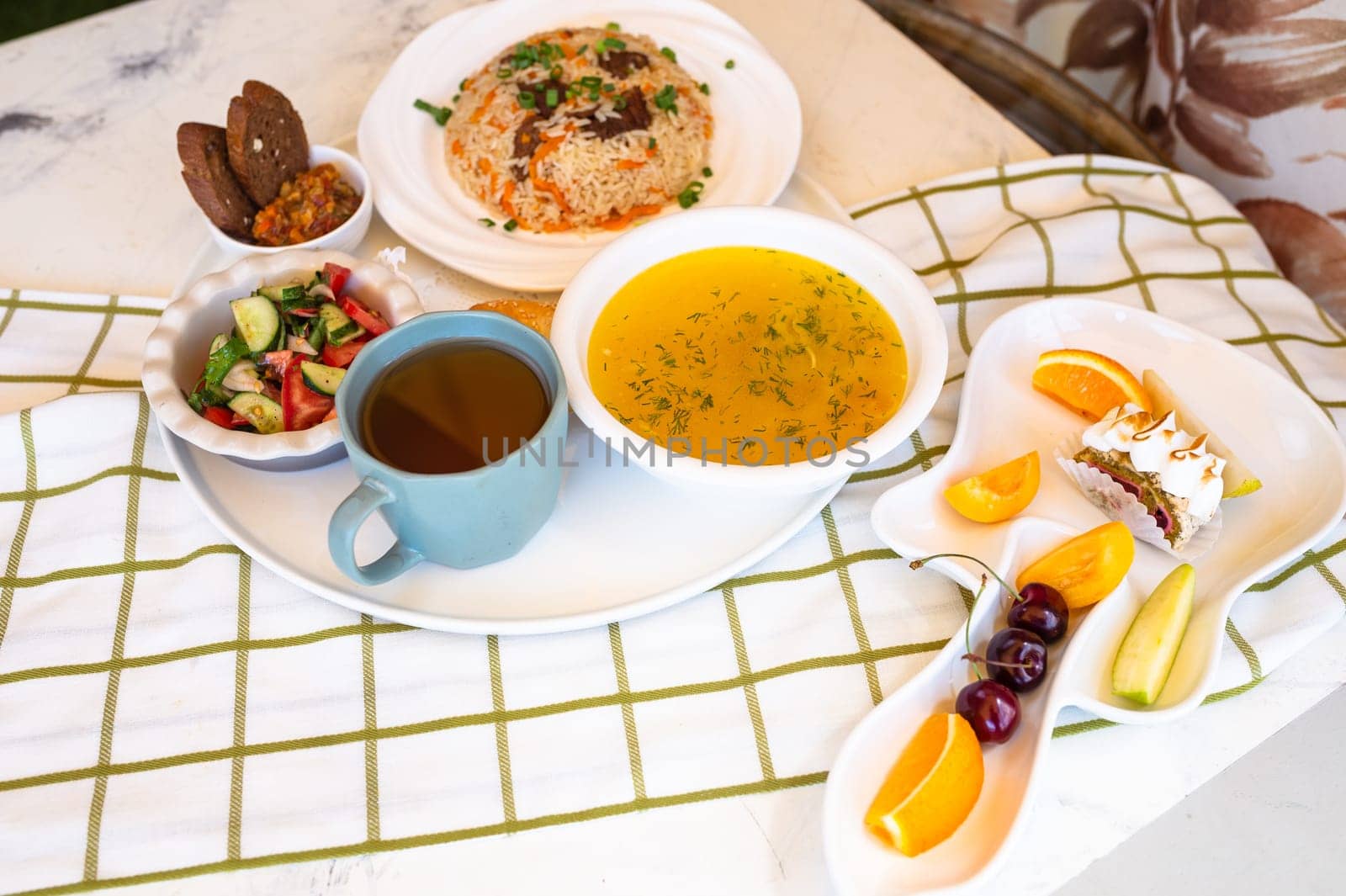 Uzbek national dishes, plov, shurpa, salad, and non on a tray with tea. Traditional Uzbek food. Checkered tablecloth background.