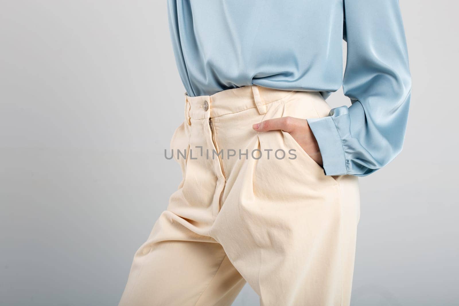 Elegant woman in pleated beige pants and blue blouse with hand in pocket by Pukhovskiy