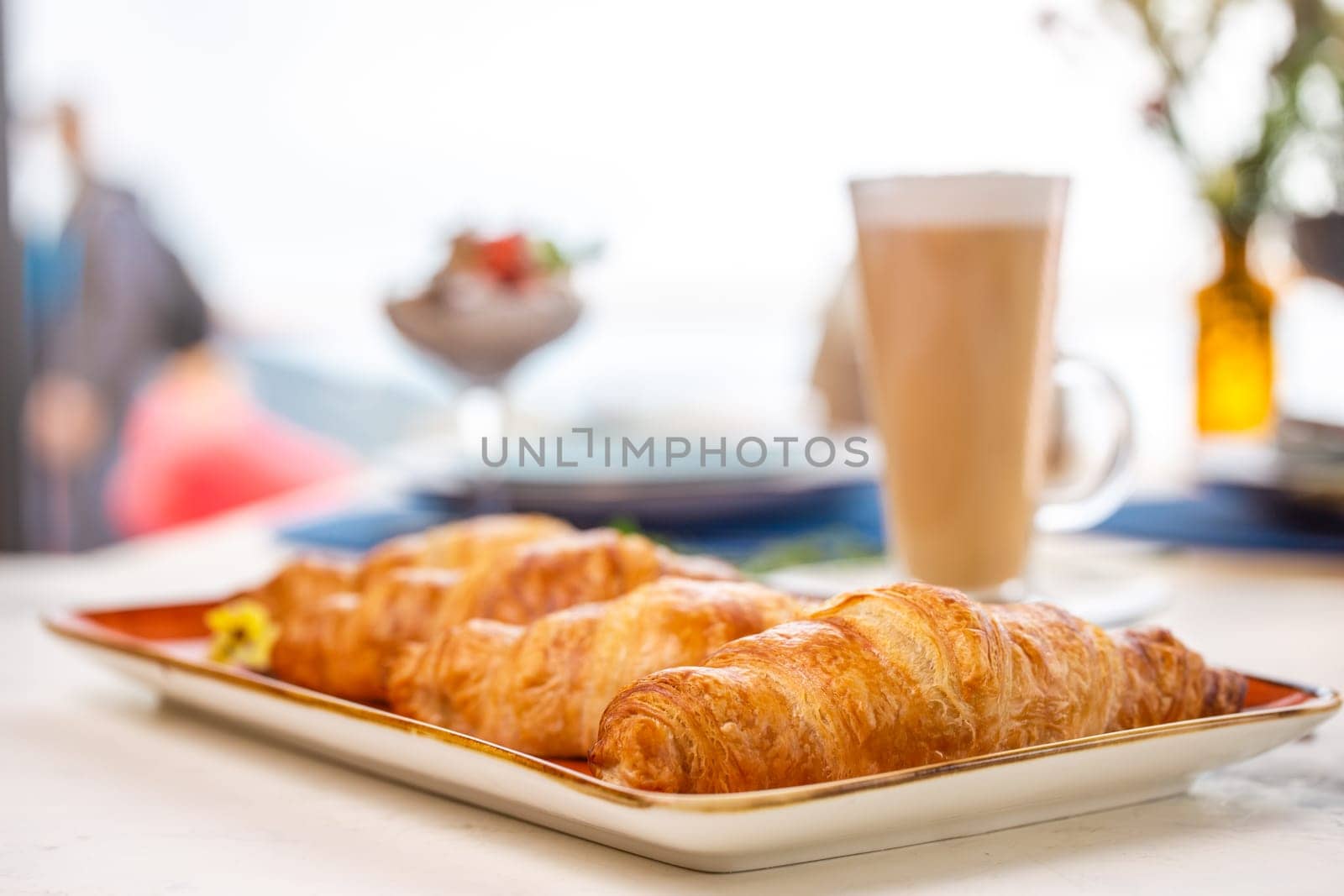 A delightful breakfast with croissants and coffee on a marble table. Croissants are golden brown on an orange plate, coffee with froth.