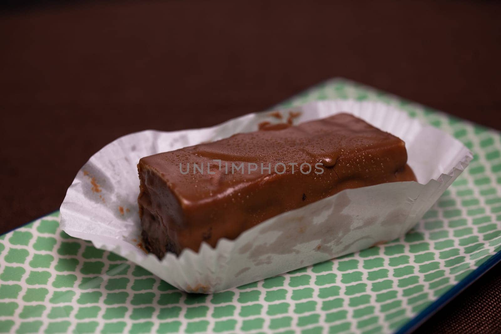 This image shows a piece of homemade chocolate fudge resting on a white paper wrapper on a light green textured background.