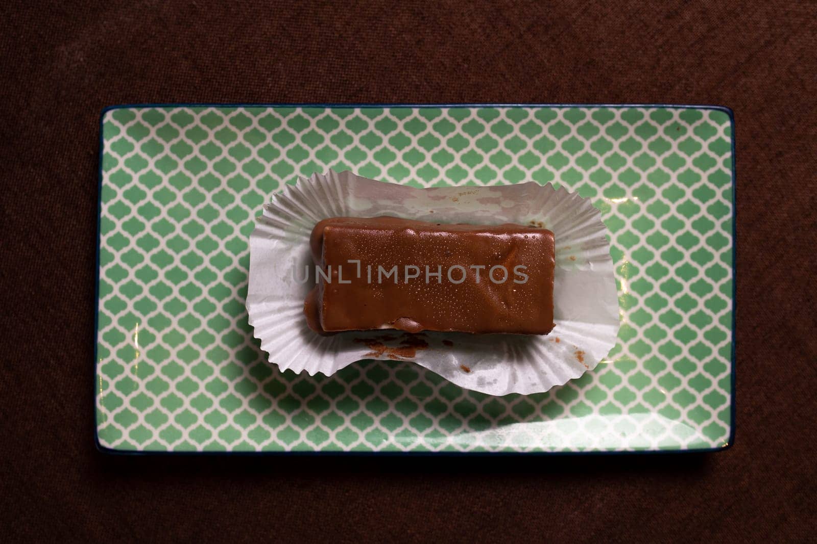 This image shows a piece of homemade chocolate fudge resting on a white paper wrapper on a light green textured background.