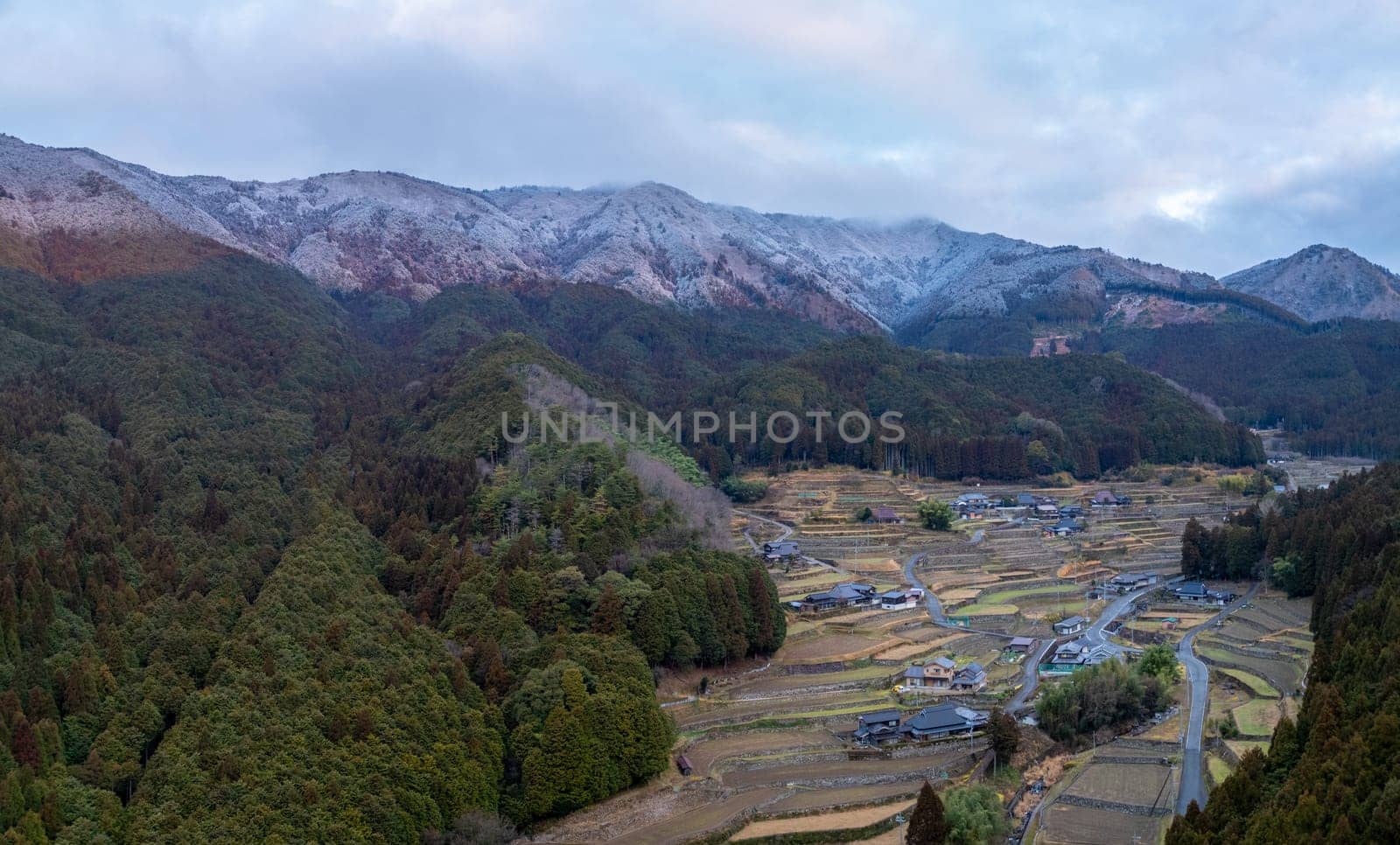 Terraced rice fields, houses, and snowy mountains in winter landscape by Osaze