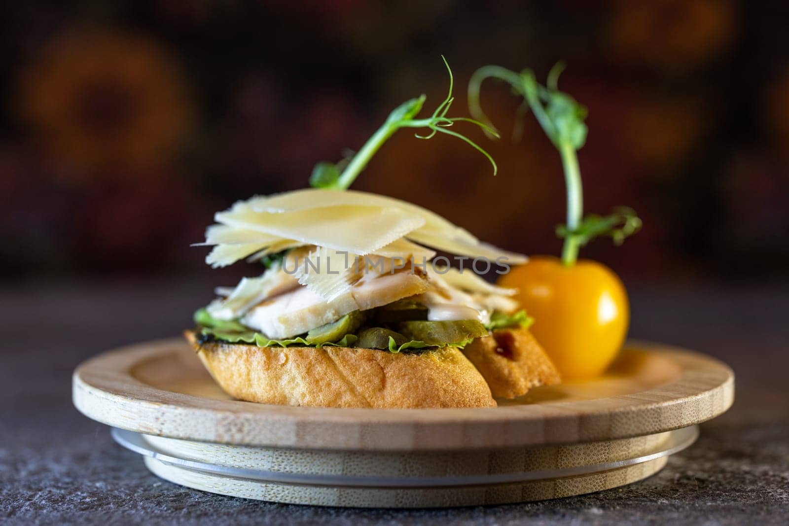 A bruschetta with chicken, pesto, and parmesan. The bruschetta is garnished with microgreens and a pea pod.