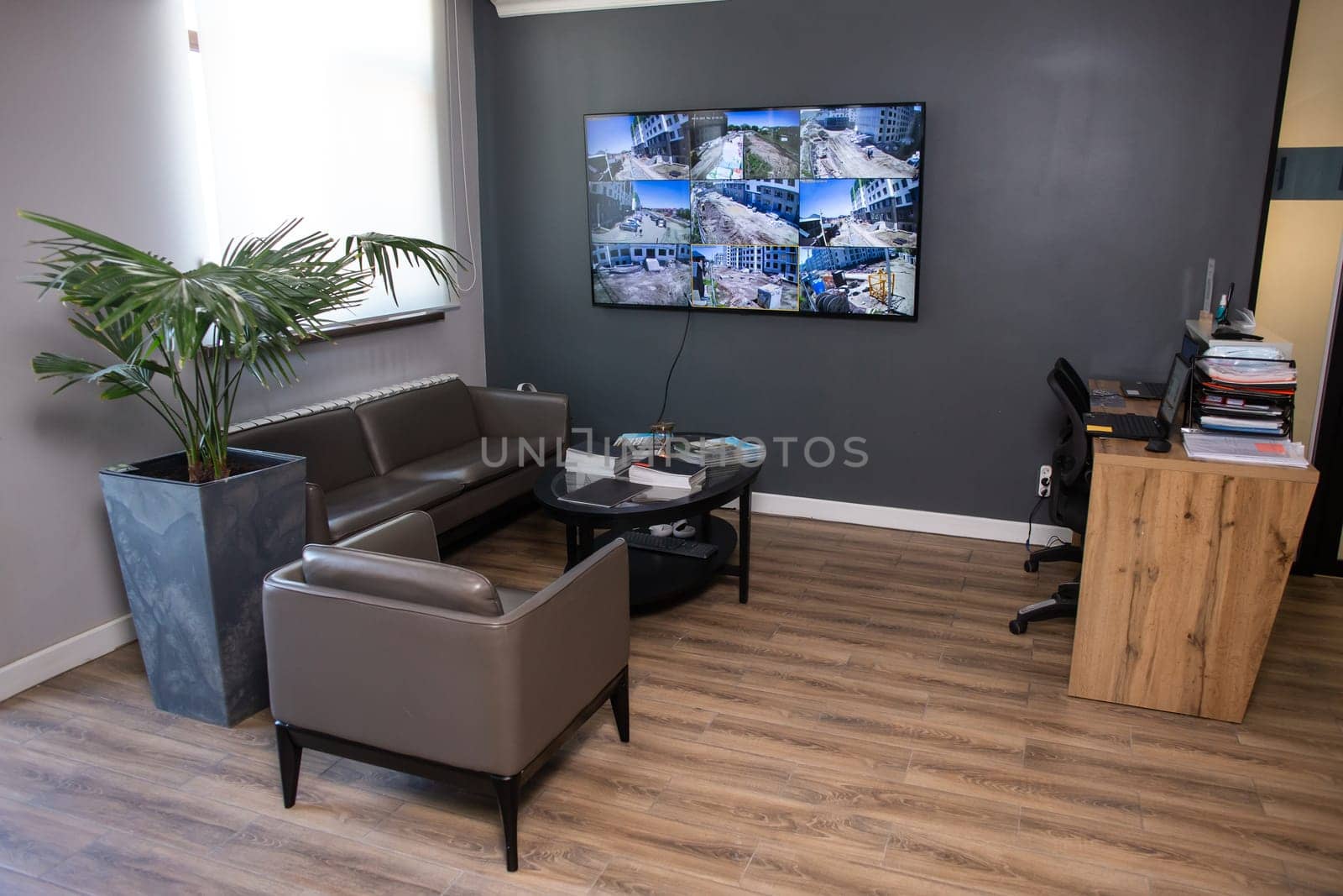 A stylish and modern office interior with dark gray walls, a large window and a monitor on the wall. comfortable leather furniture.