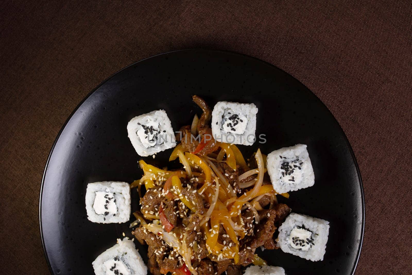 Japanese cuisine, rice rolls with sesame seeds and soy sauce on a black plate.