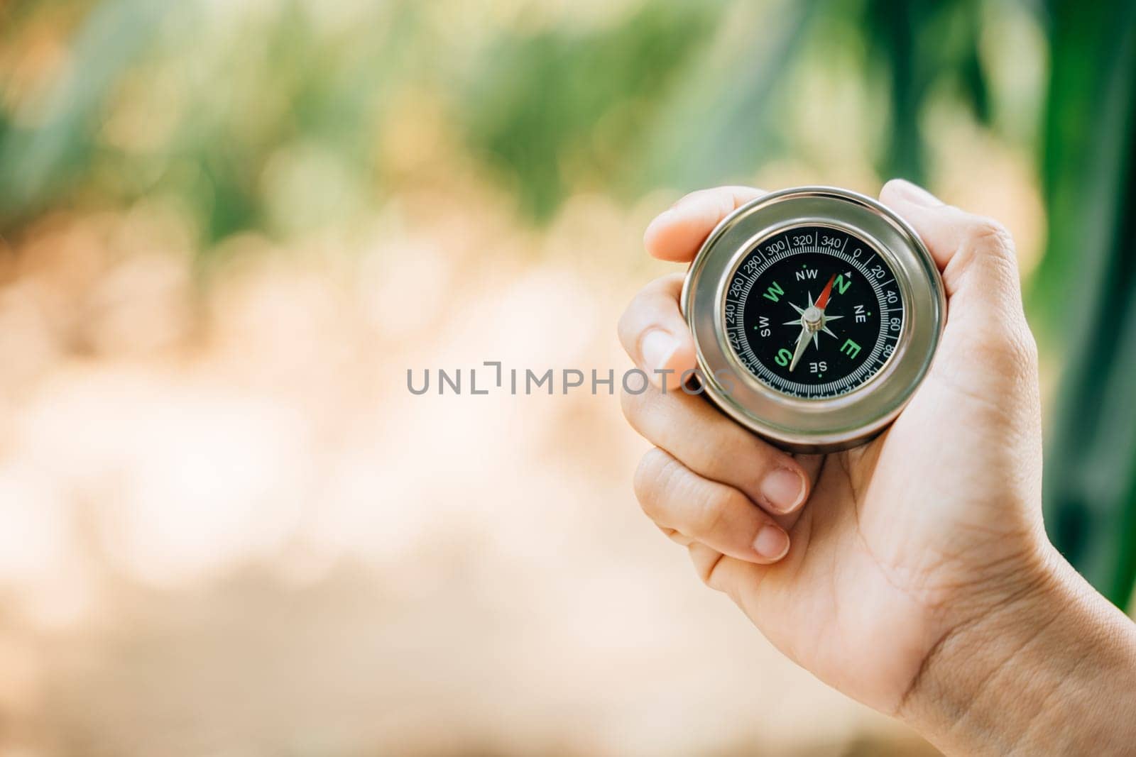 Hiker seeks direction in the forest holding a compass to overcome confusion. The compass in the traveler hand represents exploration and finding one way in the wilderness. by Sorapop