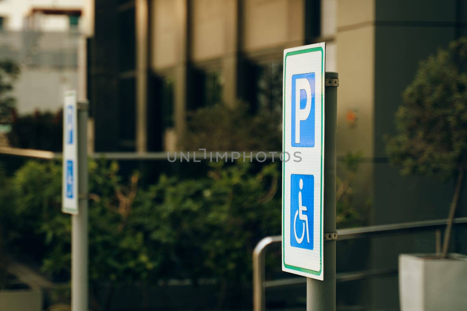 A street sign in electric blue font marks the reserved handicapped parking spot in front of the building on the grassy city road