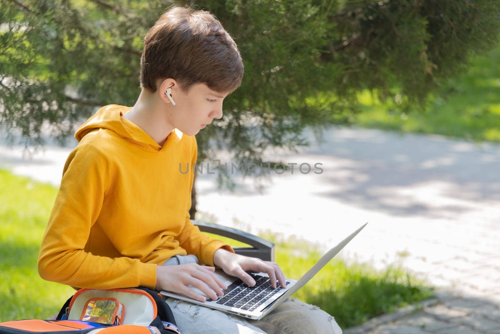 Thoughtful teenager boy working on laptop. Holding and using a laptop for networking on a sunny spring day, outdoors. by Ri6ka