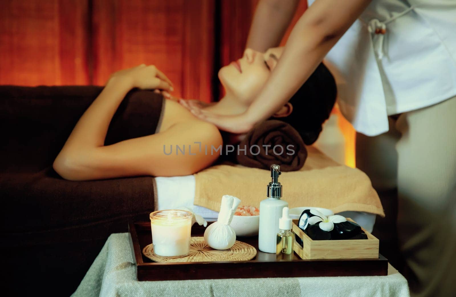 Aromatherapy massage ambiance or spa salon composition setup with focus decor candles and spa accessories on blurred woman enjoying blissful aroma spa massage in resort or hotel background. Quiescent