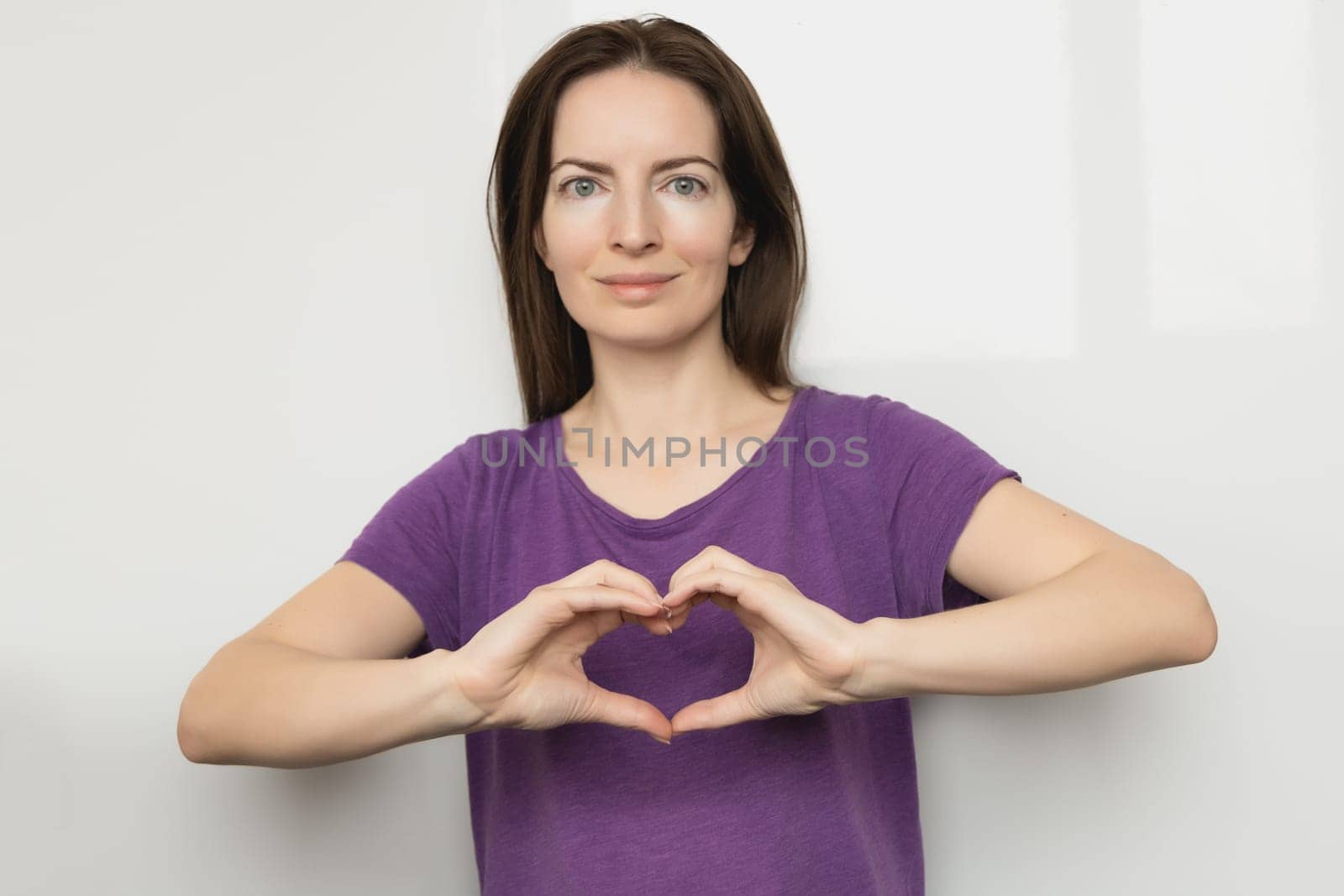 Inspire inclusion. Woman holding her hands in the shape of a heart and holding them in front of her, dressed purple t-shirt. International women's day concept. by Ri6ka