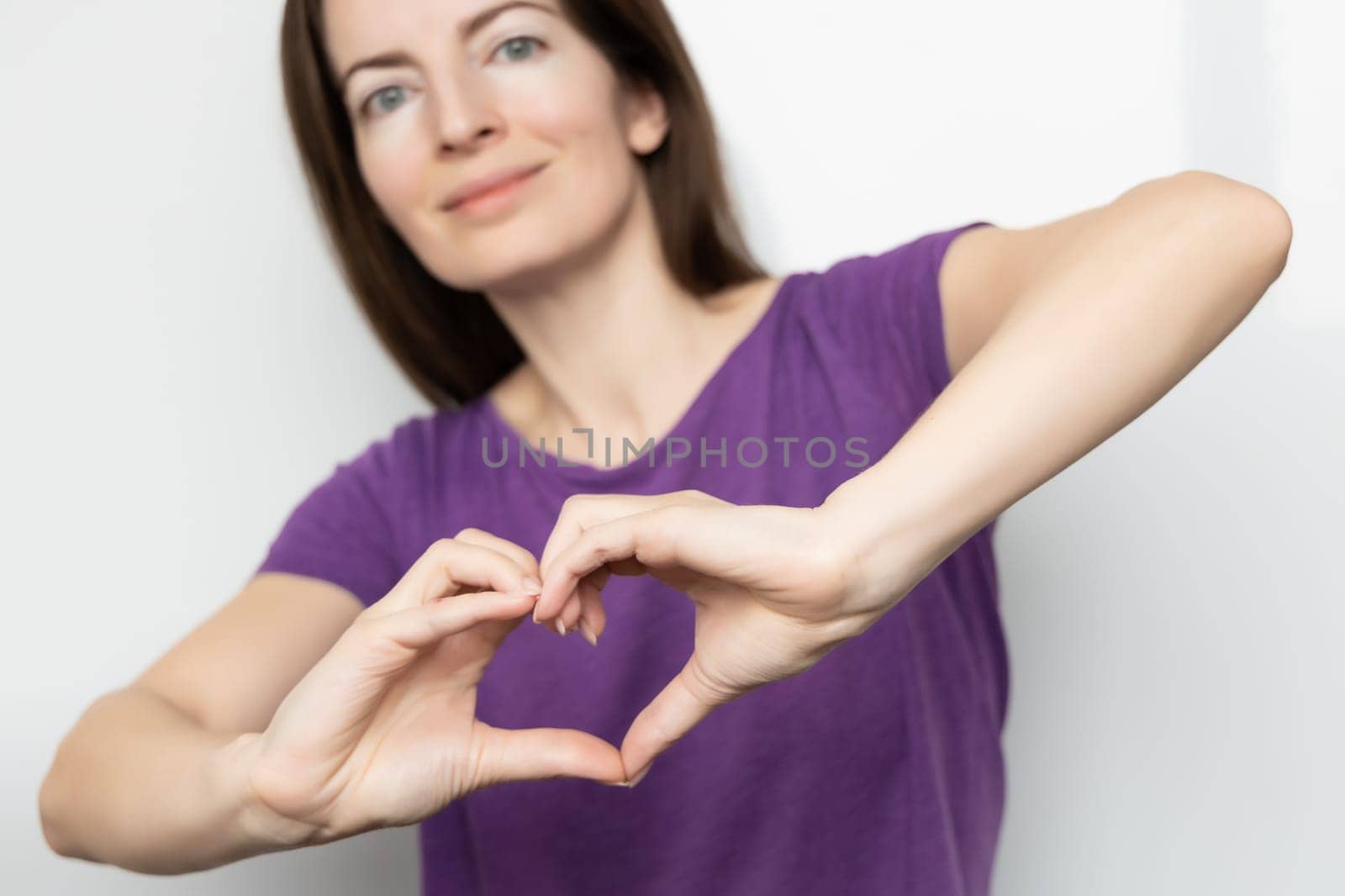 Inspire inclusion. Woman holding her hands in the shape of a heart and holding them in front of her, dressed purple t-shirt. International women's day concept