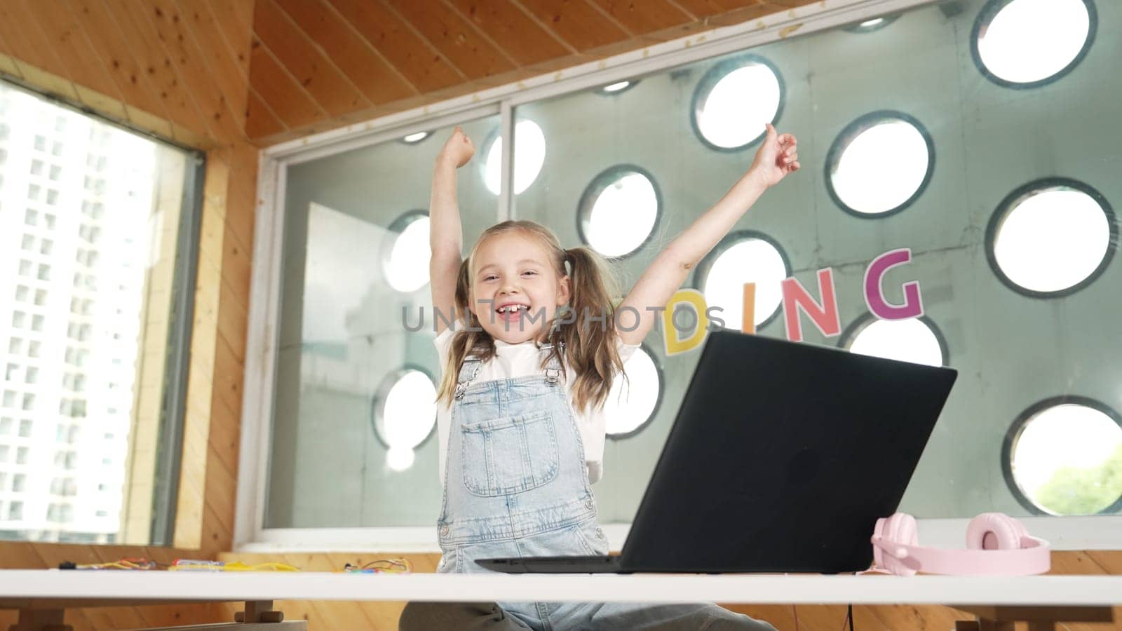 Happy girl looking at camera while raised hands to celebrate success project. Smart cute student finish writing, programing system and shouting with happiness in STEM technology class work. Erudition.