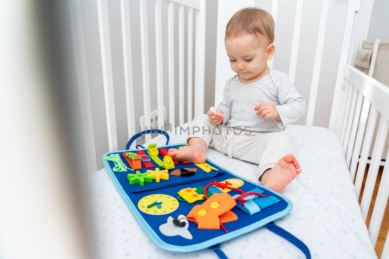 Baby playing with montessori busy book sitting in crib. Educational books and quiet books concept. Montessori busy board by Mariakray