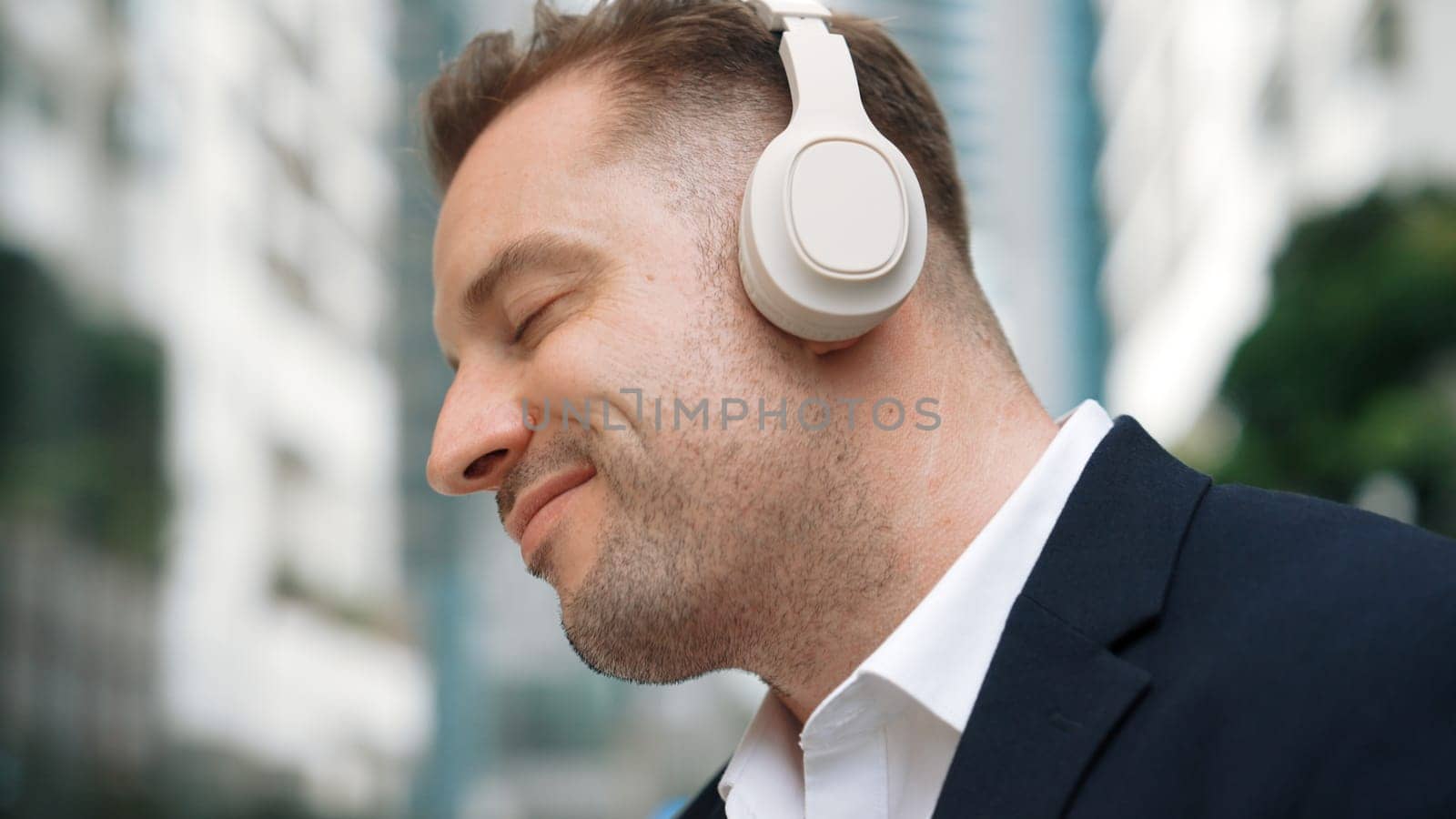 Close up of businessman listen headphone and dancing to relaxing music with cheerful and motivation. Skilled project manager enjoy to listen relaxed song with blurred background at urban city. Urbane.