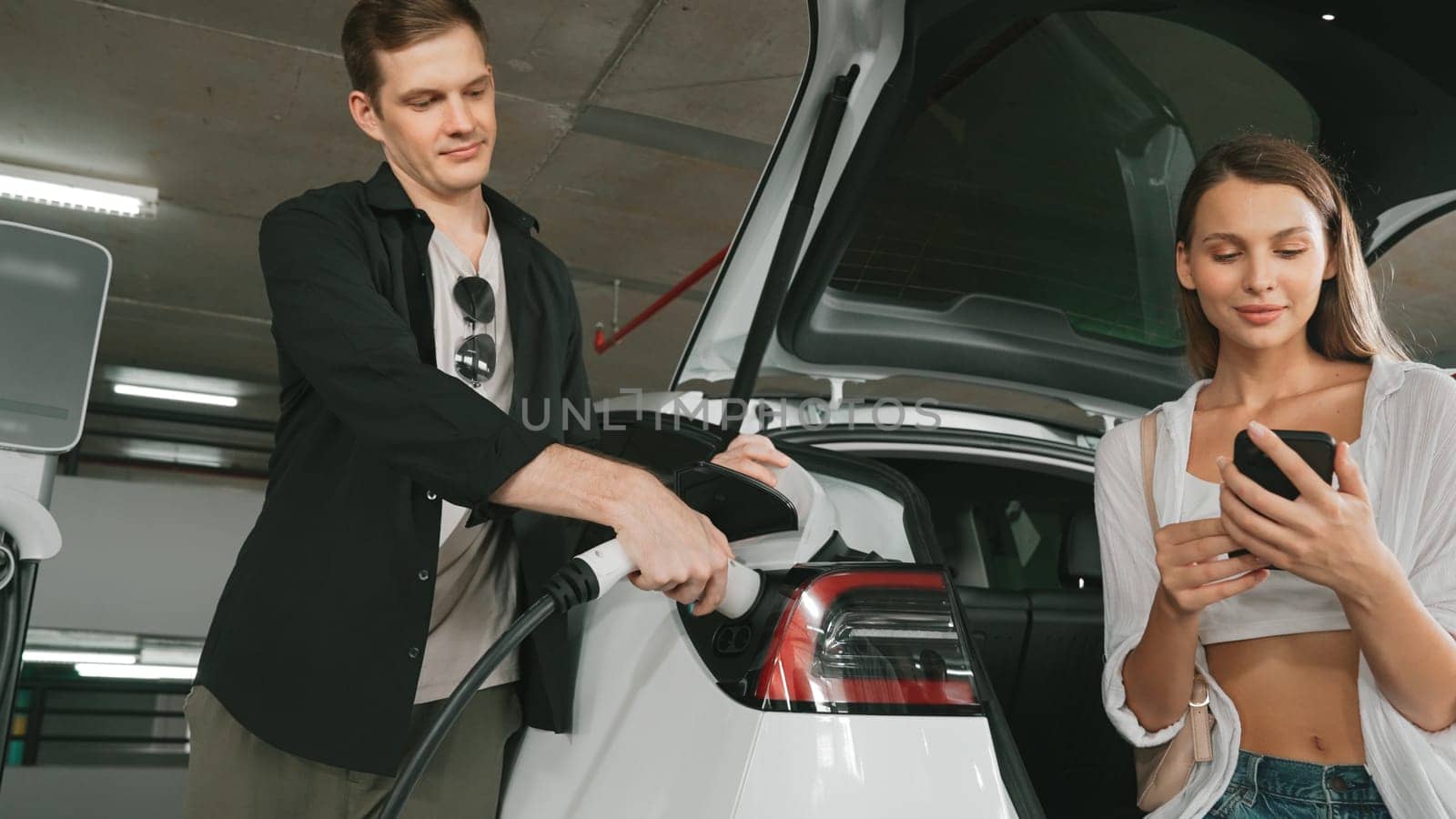 Electric car driver checks battery charging status app screen in car innards by biancoblue