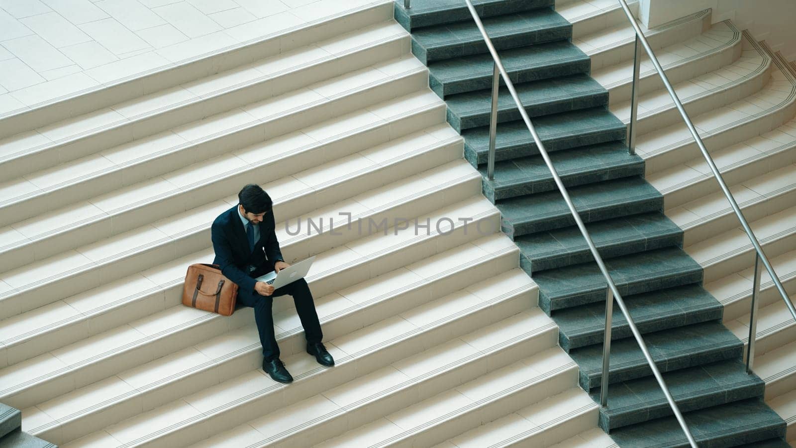 Top view of investor working or planing strategy by using laptop at stair. Professional business man wearing suit while working and typing data analysis by using laptop at modern hotel. Exultant.
