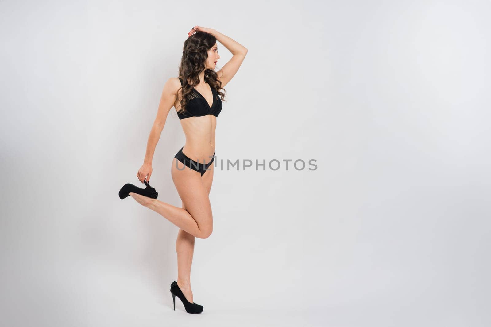 Cute brunette female model posing, wearing black and red underwear in a white studio