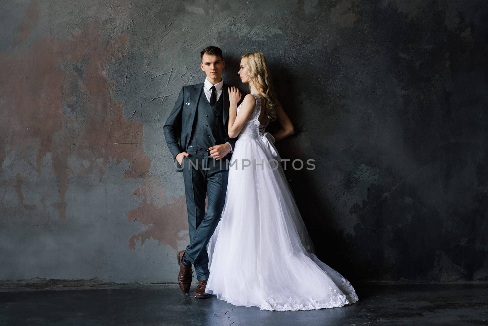 Cute wedding couple in the interior of a classic studio. They kiss and hug each other.