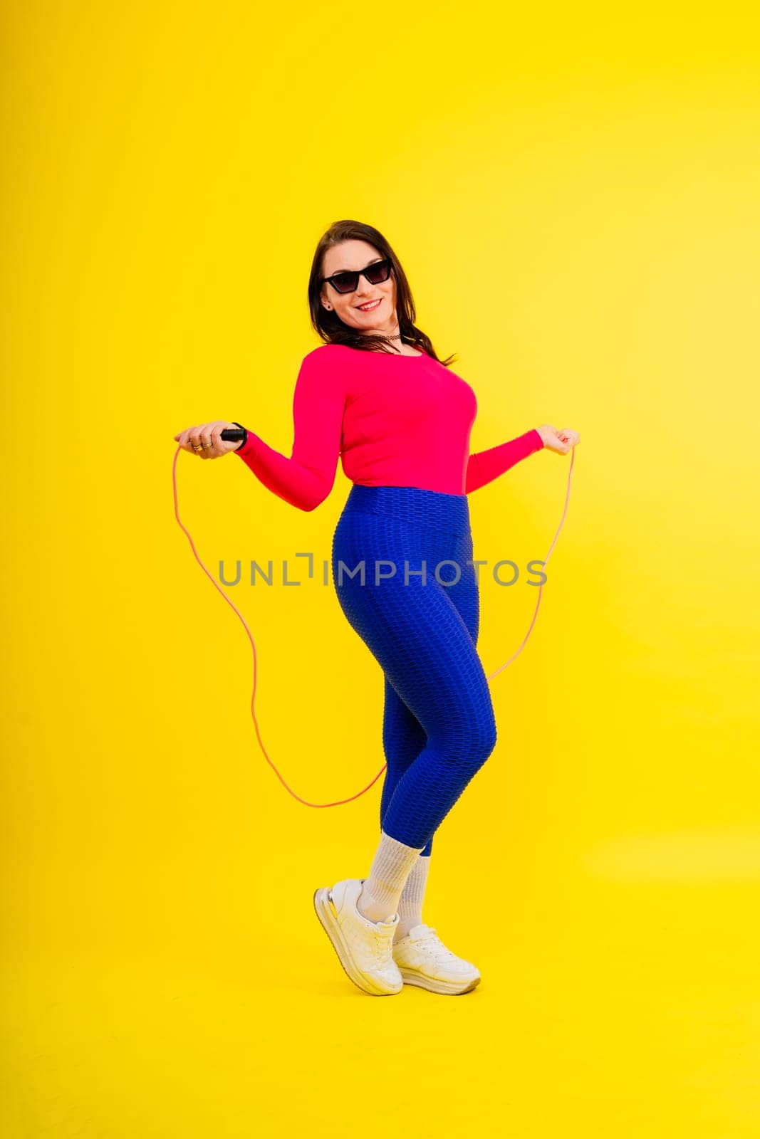 Pretty smiling plump female in a sporty top and leggings holding jumping rope in hands