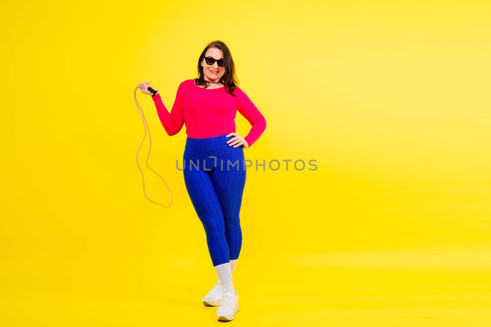 Pretty smiling plump female in a sporty top and leggings holding jumping rope in hands