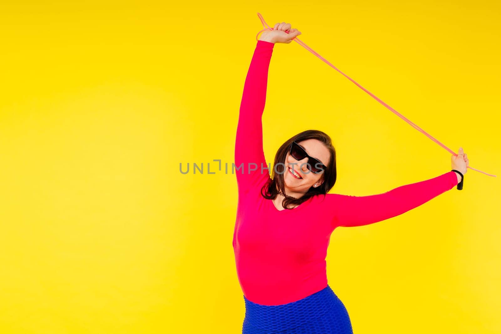 Pretty smiling plump female in sporty top and leggings holding jumping rope in hands by Zelenin