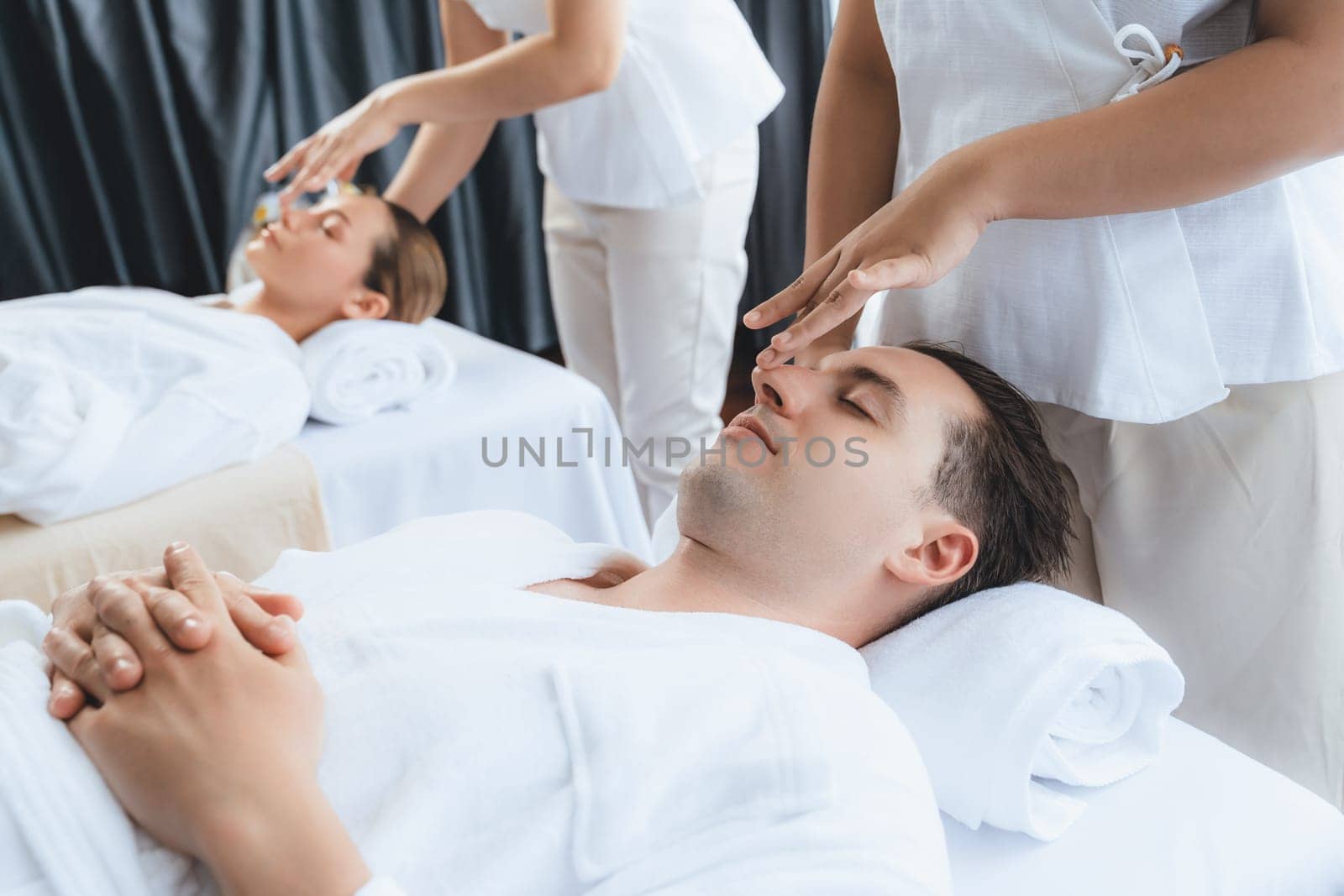 Caucasian couple enjoying relaxing anti-stress head massage and pampering facial beauty skin recreation leisure in dayspa modern light ambient at luxury resort or hotel spa salon. Quiescent