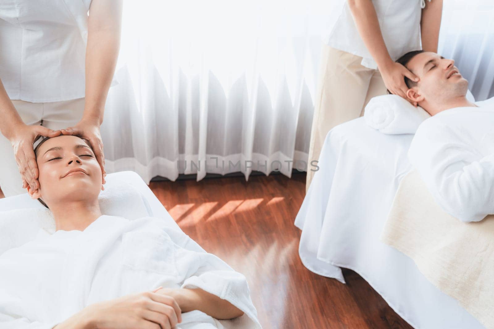 Caucasian couple enjoying relaxing anti-stress head massage and pampering facial beauty skin recreation leisure in dayspa modern light ambient at luxury resort or hotel spa salon. Quiescent