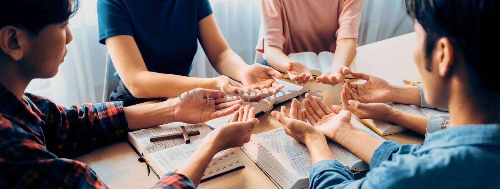 Cropped image of diversity people hand praying together at wooden church on bible book. Group of believer hold hand together faithfully. Concept of hope, religion, faith, god blessing. Burgeoning.