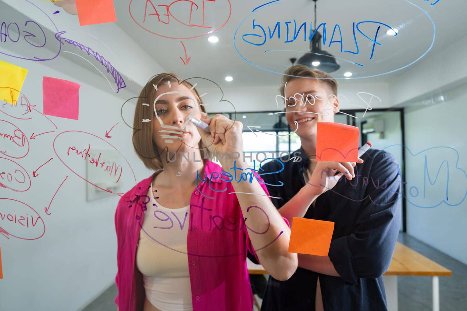 Couple of young creative start up business people brainstorming idea and solving problems by using sticky note and mind map at glass board, meeting room. discussing, working together. Immaculate.