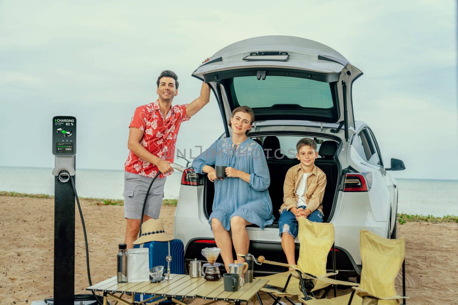 Family vacation trip traveling by the beach with electric car, happy family recharge EV car, enjoying outdoor camping coffee. Seascape travel and eco-friendly car for clean environment. Perpetual